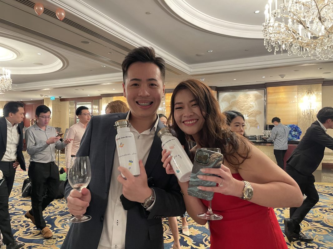 Two happy customers at a Dinner and Dance event holding their finalized customized water bottles created by Partyinkers. They smile for the camera, showcasing the personalized products, which represent the future of personalized games and experiences at events.