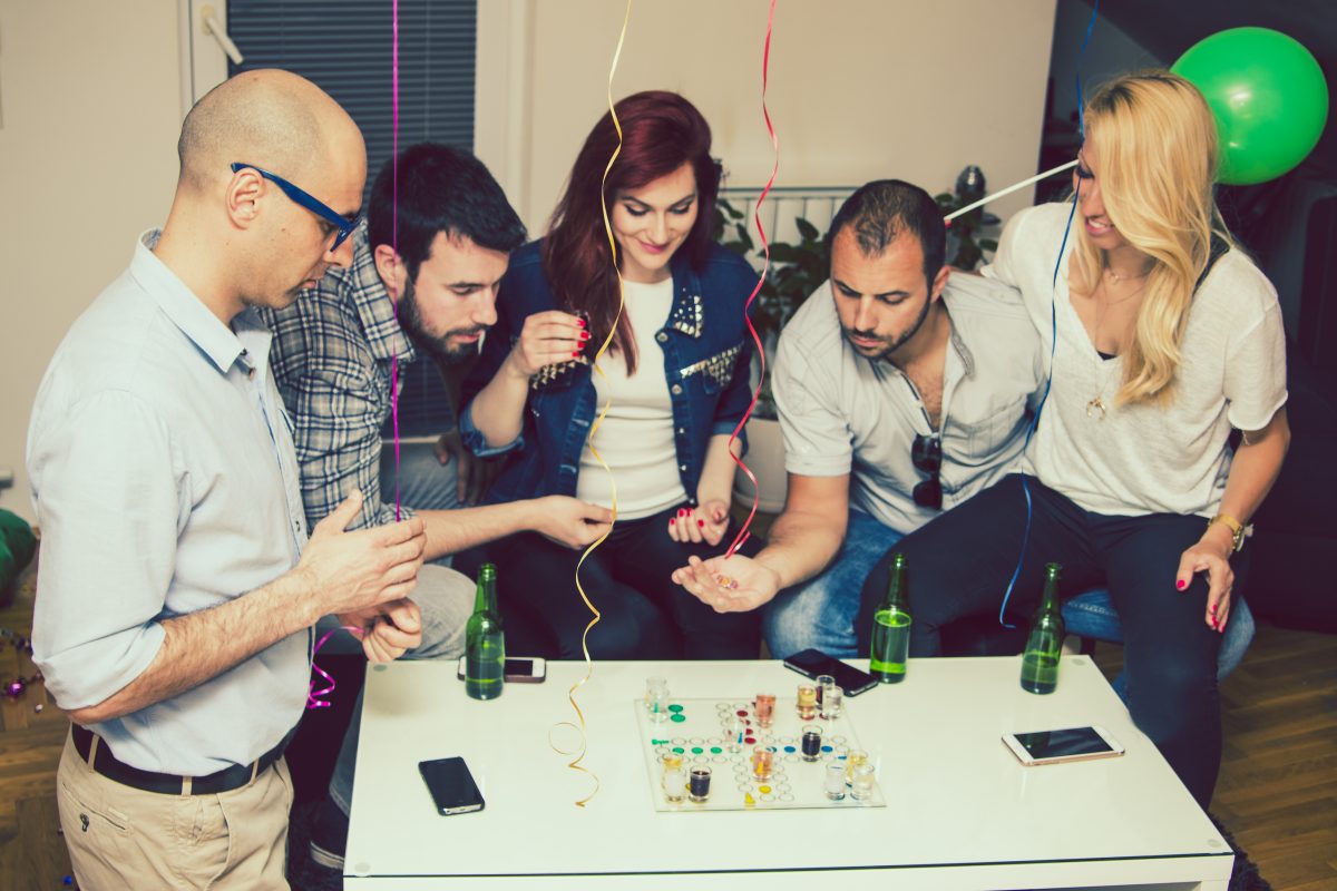 A group of adults engaged in a fun board game at a Dinner and Dance event. The setting includes festive decorations, drinks, and a casual atmosphere, showcasing interactive icebreaker games that promote engagement and connection among attendees.