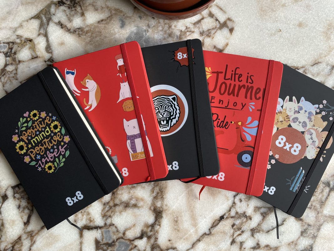 A collection of custom-designed notebooks with unique illustrations and personalized branding, representing the 'Prize-Based Games with Instant Customization' section. These personalized items highlight the excitement and creativity involved in instant customization at Dinner and Dance events, where attendees can walk away with one-of-a-kind prizes