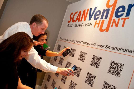 Participants enthusiastically scanning QR codes on a wall during a scavenger hunt at an event, representing the 'Scavenger Hunt with Personalized Finisher Gifts' section. This interactive activity combines technology with fun, rewarding winners with personalized gifts that enhance the experience