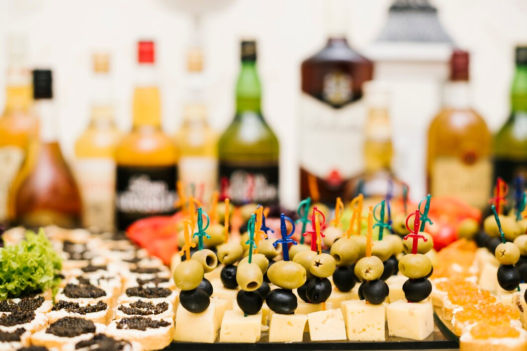 A colorful arrangement of appetizers featuring cheese cubes, olives, and caviar-topped bread, with an assortment of liquor bottles.
