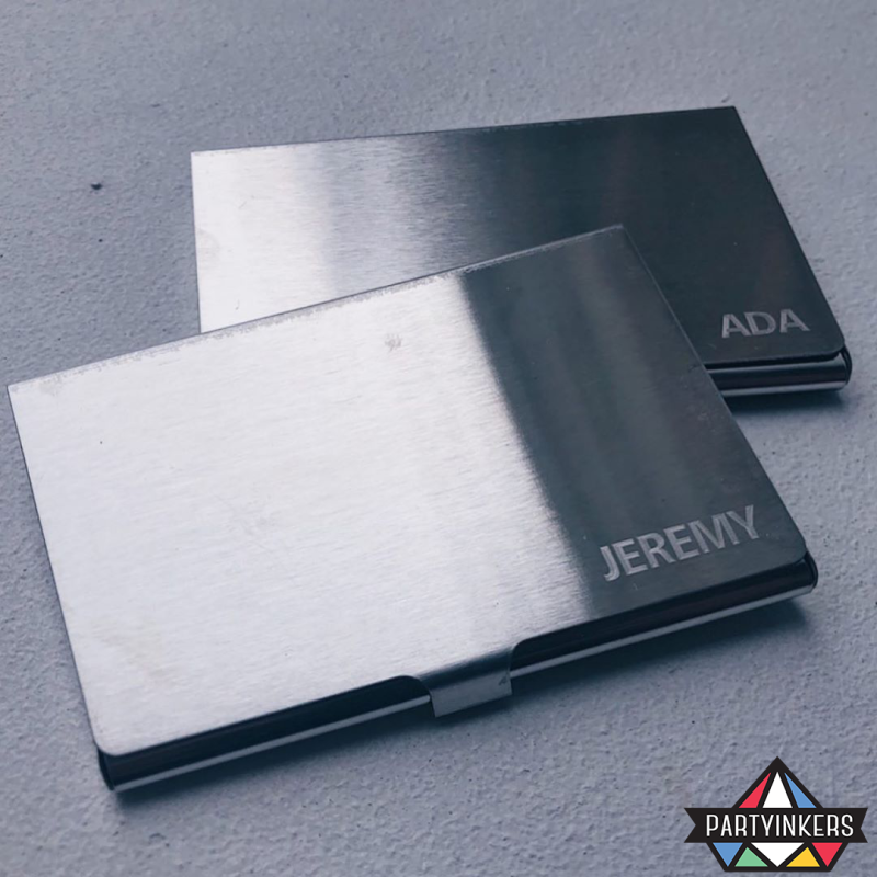 Two sleek, personalized metal cardholders with engraved names, representing the 'VR Challenges with Laser-Engraved Rewards' section. These custom laser-engraved rewards highlight the innovative and personalized touch that Partyinkers brings to events, making them perfect prizes for participants of virtual reality challenges.
