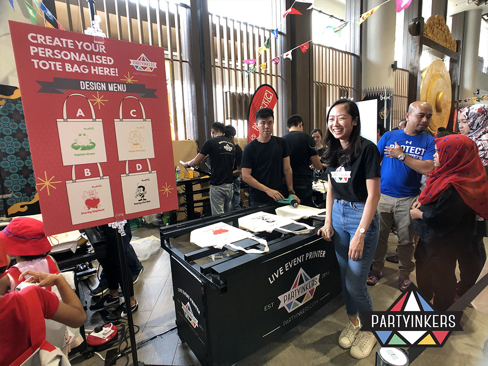 A lively interactive swag booth at an event where attendees can personalize tote bags with custom designs as conference gifts for attendees, showcasing the engaging experience provided by Partyinkers' live event printing service