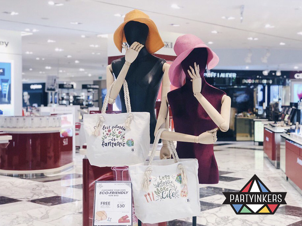 Mannequins at the Robinsons event displaying eco-friendly tote bags with custom designs as conference gifts for attendees promoting sustainable swag options created through Partyinkers' live printing service.