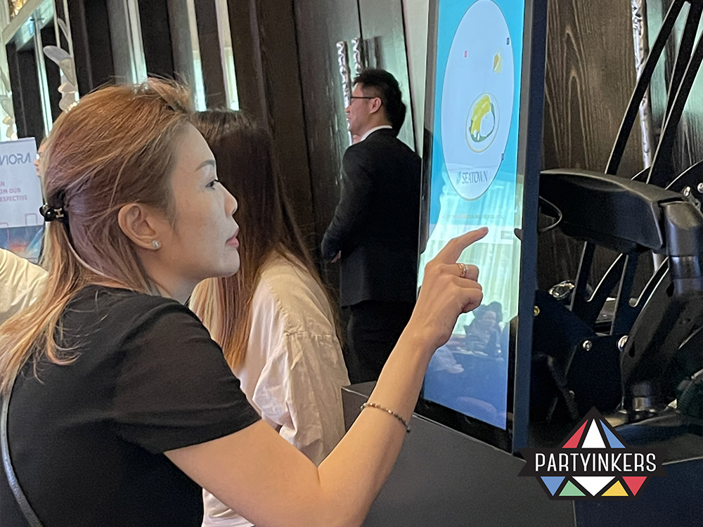 An attendee at the Seatown event using a touchscreen kiosk to personalize a custom coaster with unique designs, showcasing Partyinkers' live printing service for practical and memorable swag.