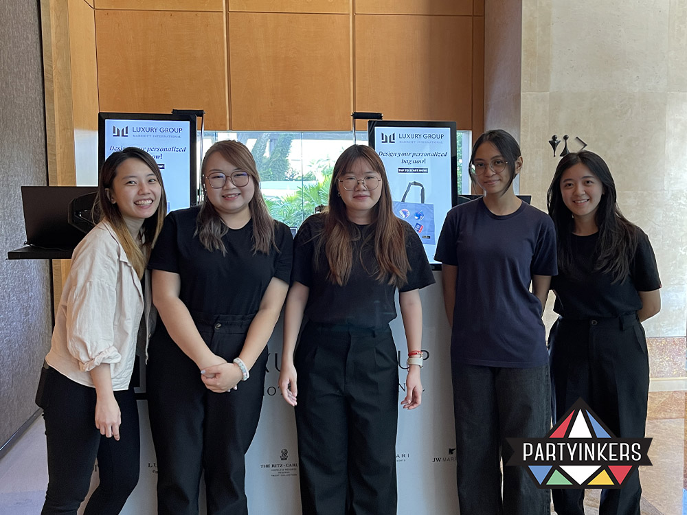The Partyinkers team standing proudly in front of their interactive booth at a corporate event, ready to provide live personalized printing services as conference gifts for attendees
