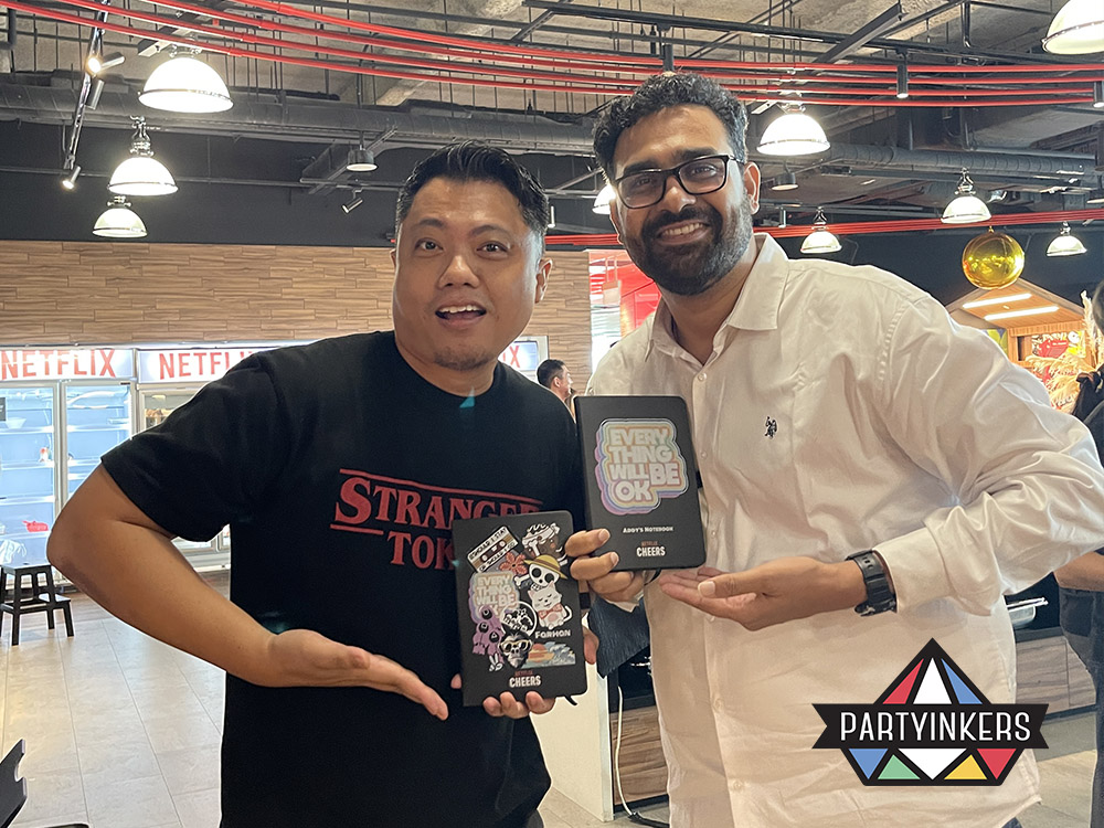 Two attendees from the Netflix Cheers event proudly displaying their personalized notebooks with custom designs, created using Partyinkers' live printing service.
