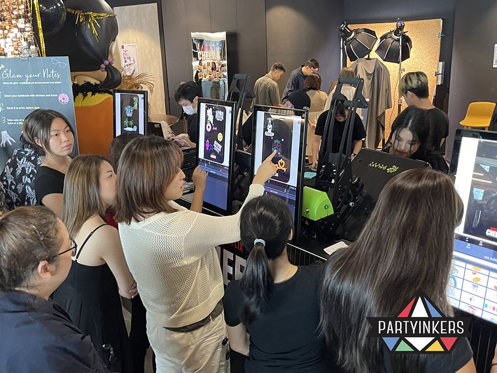 Attendees at the Netflix Cheers event using touchscreen kiosks to design and personalize their notebooks with custom graphics, showcasing Partyinkers' live printing service.