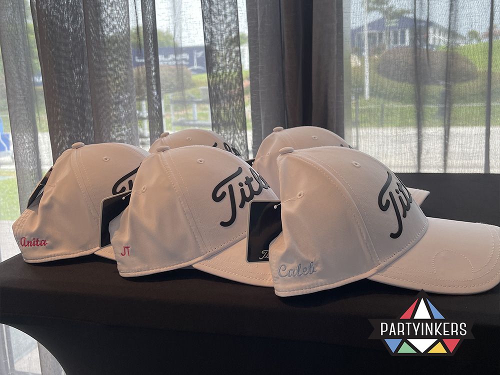 A display of personalized embroidered caps featuring attendees' names, created as conference gifts for attendees at a conference using Partyinkers' live embroidery service.