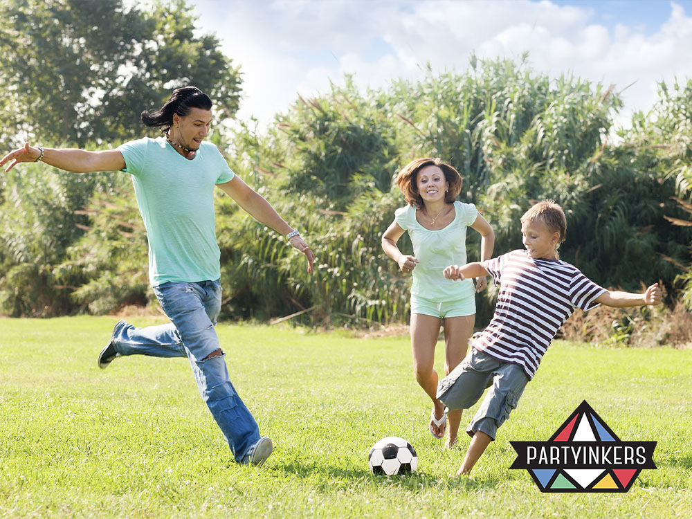 A family playing soccer together outdoors during a corporate family day activities, enjoying a friendly sports competition.