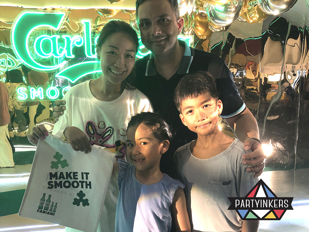 A family posing with a custom-designed tote bag at the Carlsberg Gastrobeats event during a corporate family day, showcasing the fun and interactive carnival atmosphere with live printing stations.