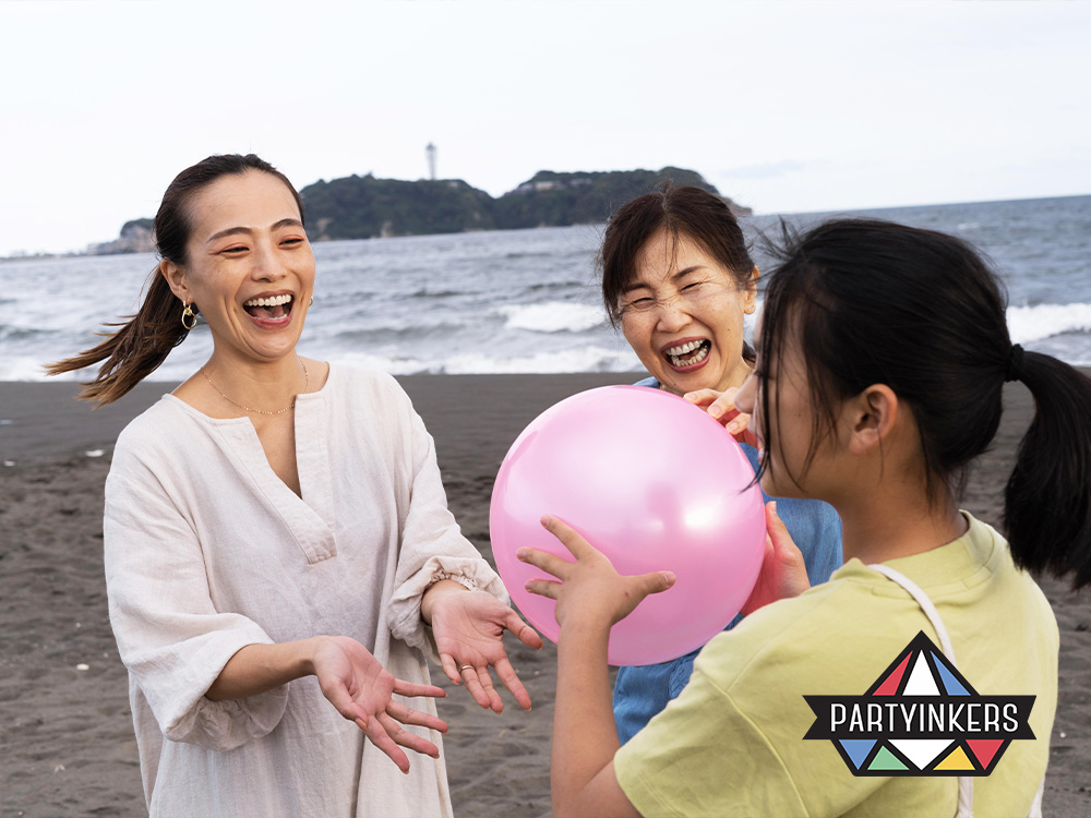 A family laughing and playing with a balloon on the beach during a corporate family day activities, celebrating the tradition of fun and togetherness
