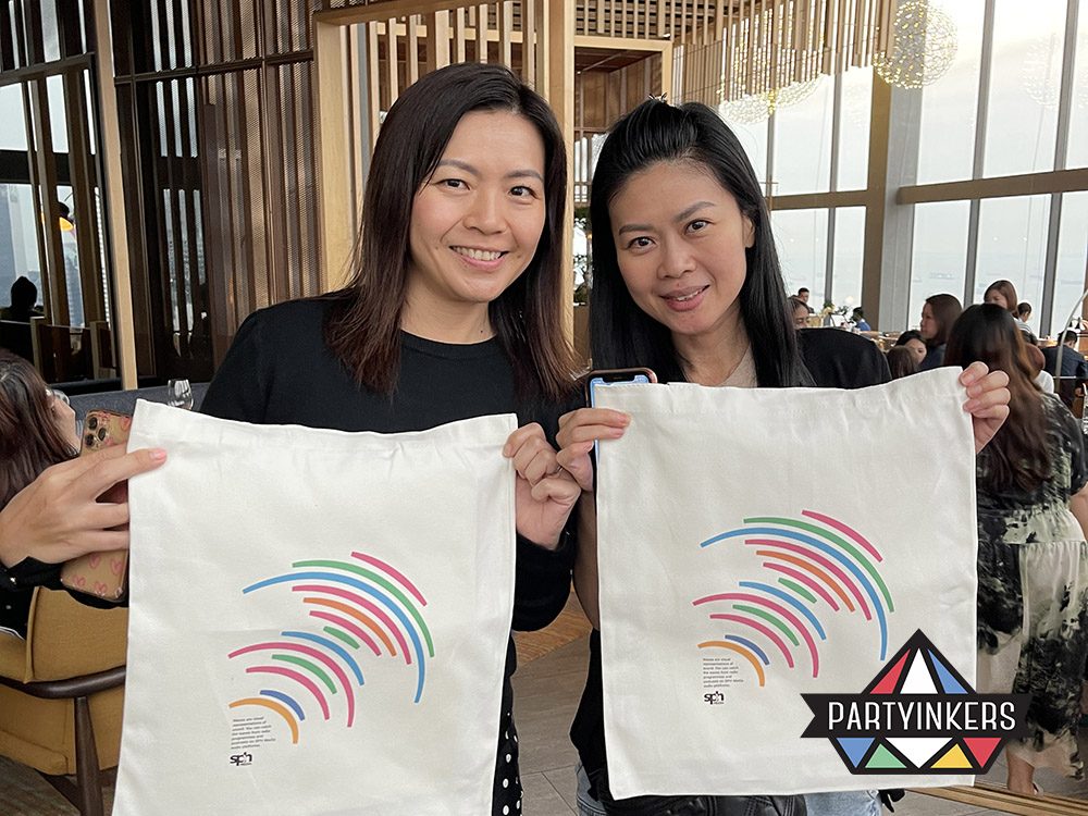 Two attendees proudly displaying personalized tote bags received as giveaways at an event. High-impact giveaways like custom-designed tote bags encourage engagement and provide attendees with memorable, practical keepsakes.