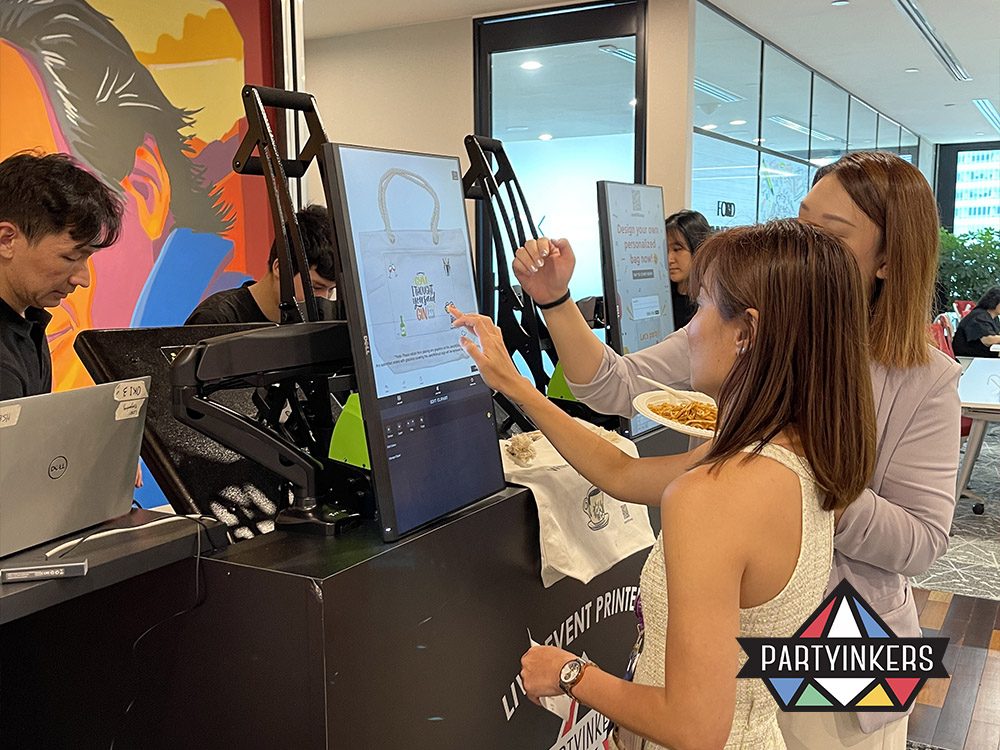 Attendees using a large touchscreen at a Partyinkers booth to design personalized products in real time. This interactive technology enhances event engagement by allowing participants to create custom items and view their designs instantly, providing a memorable and engaging experience.