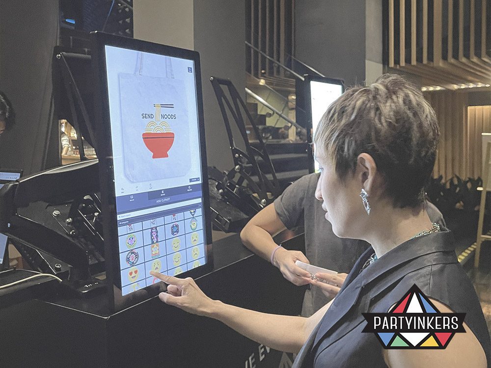 Attendees using a large touchscreen at a Partyinkers booth to design personalized products in real time. This interactive technology enhances event engagement by allowing participants to create custom items and view their designs instantly, providing a memorable and engaging experience.