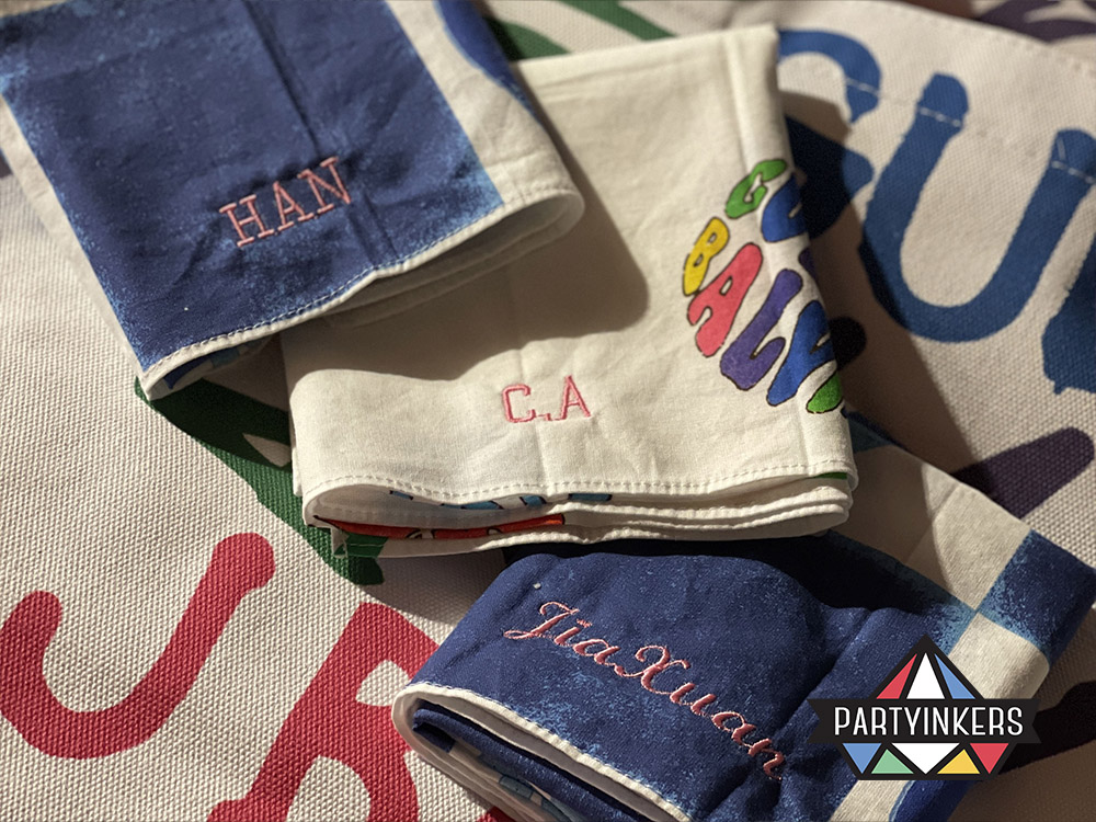Close-up of personalized embroidered napkins with names stitched onto the fabric, highlighting the premium quality and craftsmanship of customized keepsakes created through live embroidery.