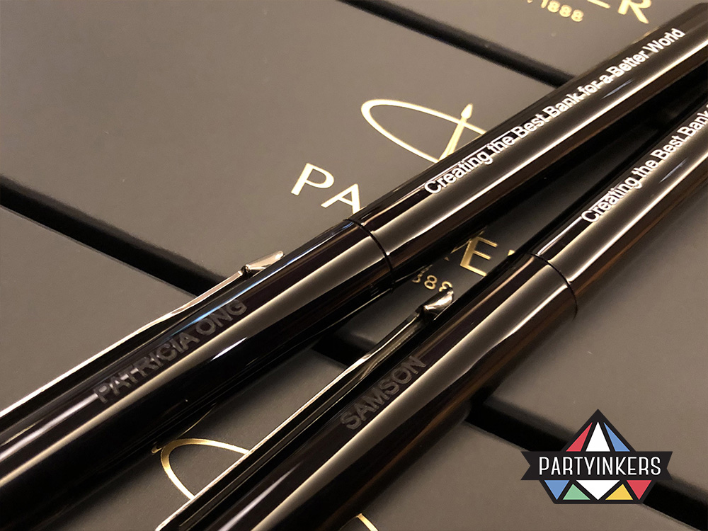 Close-up of personalized black pens engraved with attendee names and a branded message, illustrating the engaging and memorable experience of live laser engraving at a Partyinkers event.