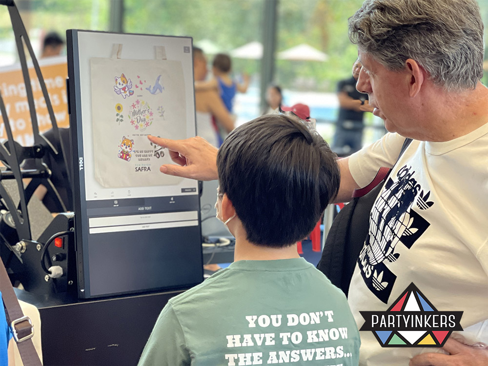 An attendee and a child customizing a tote bag design on a touchscreen interface during a live digital printing session at a Partyinkers event, illustrating the engaging and interactive experience of creating personalized products in real-time as an interactive booth ideas.