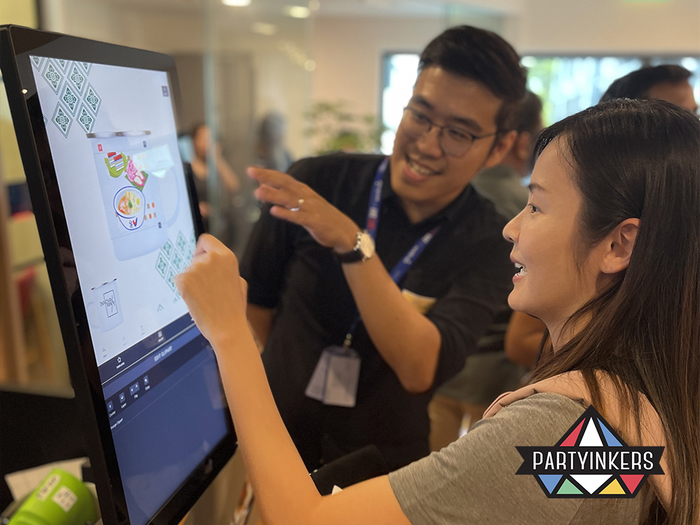 A woman interacts with a touchscreen display at a trade show booth, guided by a helpful staff member. This scene highlights the importance of incorporating interactivity into "Trade Show Booth Ideas" to engage visitors. The use of a touchscreen allows for a personalized and immersive experience, demonstrating how interactive elements can increase engagement, build trust, and create memorable connections with attendees.