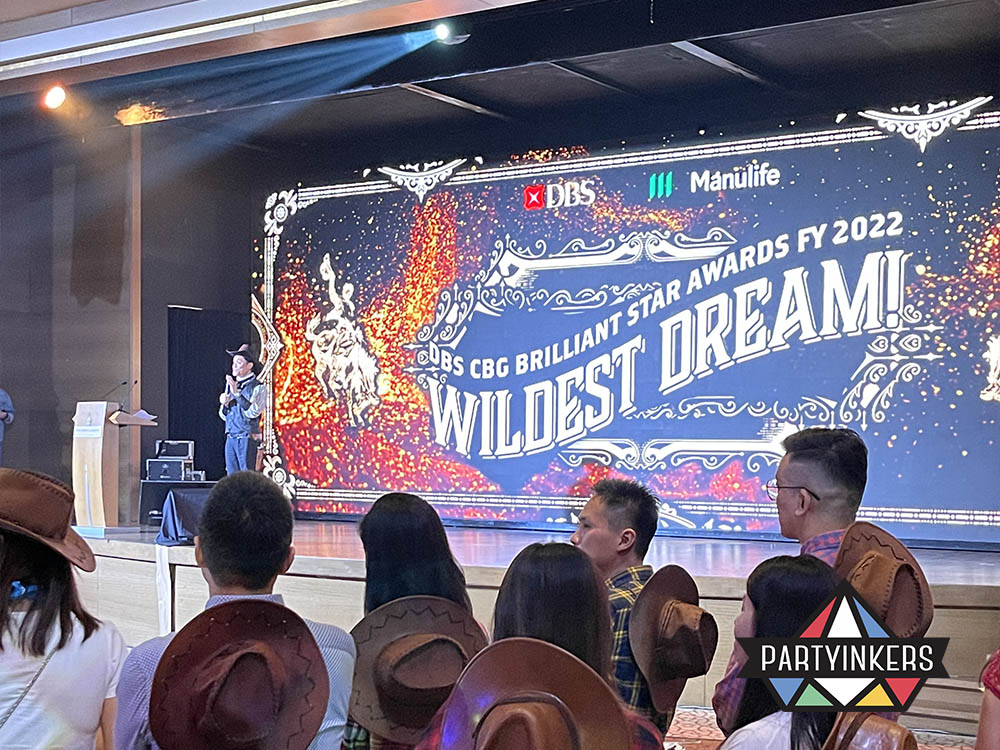 Attendees in cowboy-themed outfits watching an award presentation during the DBS CBG Brilliant Star Awards event, showcasing one of the interactive event ideas where a themed environment and live performances create an engaging and immersive experience for participants.