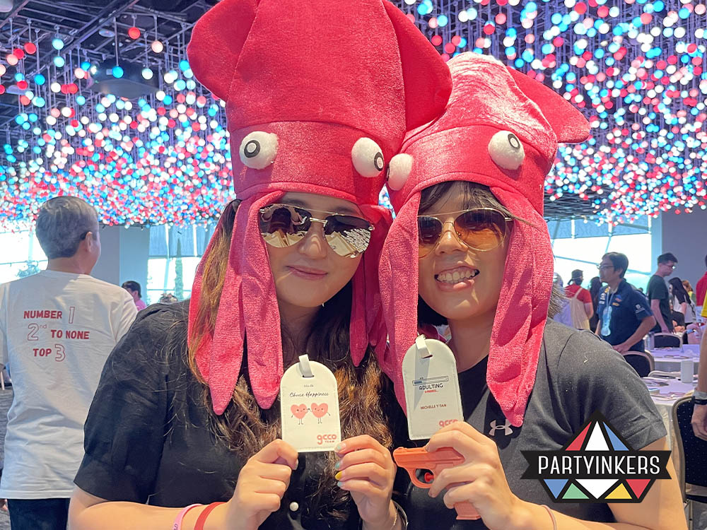 Two attendees wearing fun squid hats and holding personalized luggage tags at an event, showcasing one of the interactive event ideas where personalized items and playful accessories help enhance audience engagement and create memorable experiences.