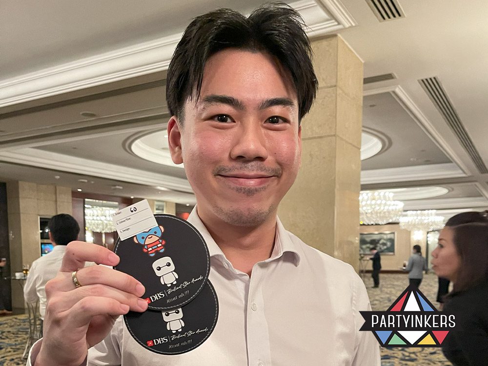 A cheerful guest holding custom-designed coasters featuring vibrant patterns, created at a Dinner and Dance theme event, showcasing personalized and memorable keepsakes.