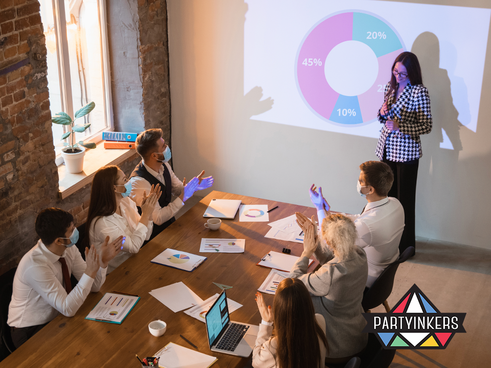 Business professionals in a meeting room clapping for a presentation with a pie chart on the wall, showcasing teamwork and analytics in event management.