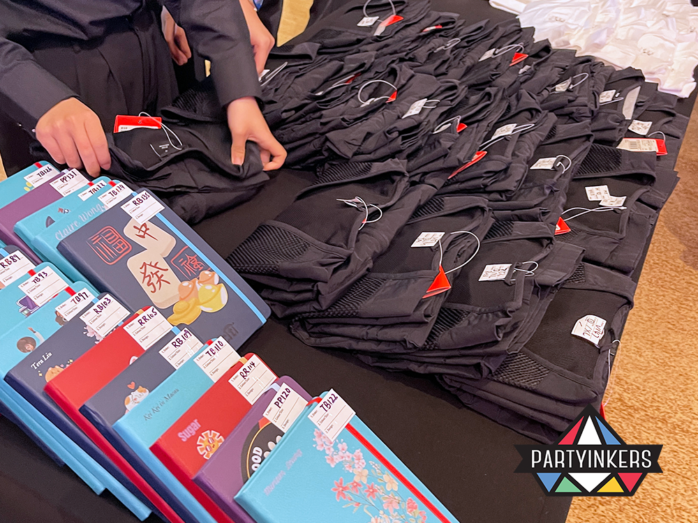 A close-up view of a table displaying customized items at a corporate event, including notebooks and vests with professionally printed and embroidered names and logos. This detail shot showcases the quality and variety of customization available to attendees.