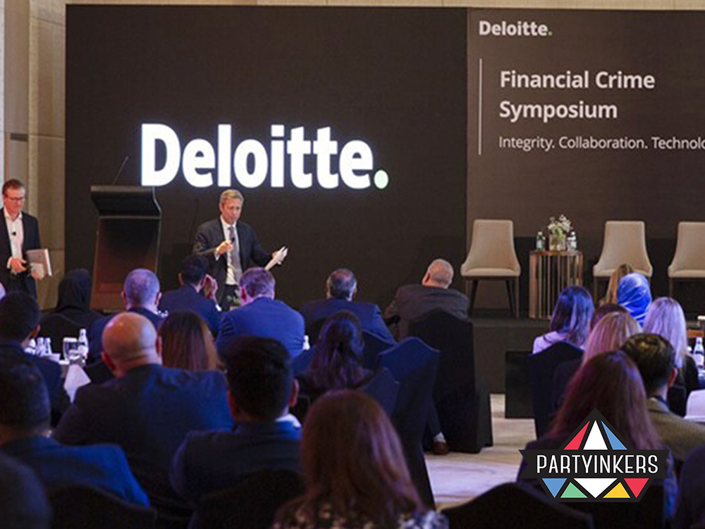 Industry professionals gather at a Deloitte symposium focused on financial crime, featuring prominent speakers discussing topics related to integrity, collaboration, and technology. The event showcases a professional setting with a focused audience and a large branded backdrop, emphasizing the serious nature of the conference themes.