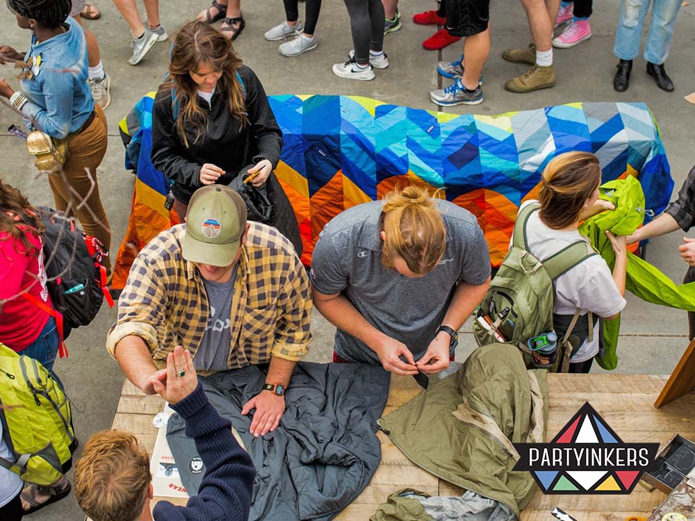 A lively outdoor event showcasing brand activation ideas, where attendees engage in hands-on customization of sustainable merchandise. A crowd gathers around a colorful booth, interacting with brand representatives to create personalized promotional items.