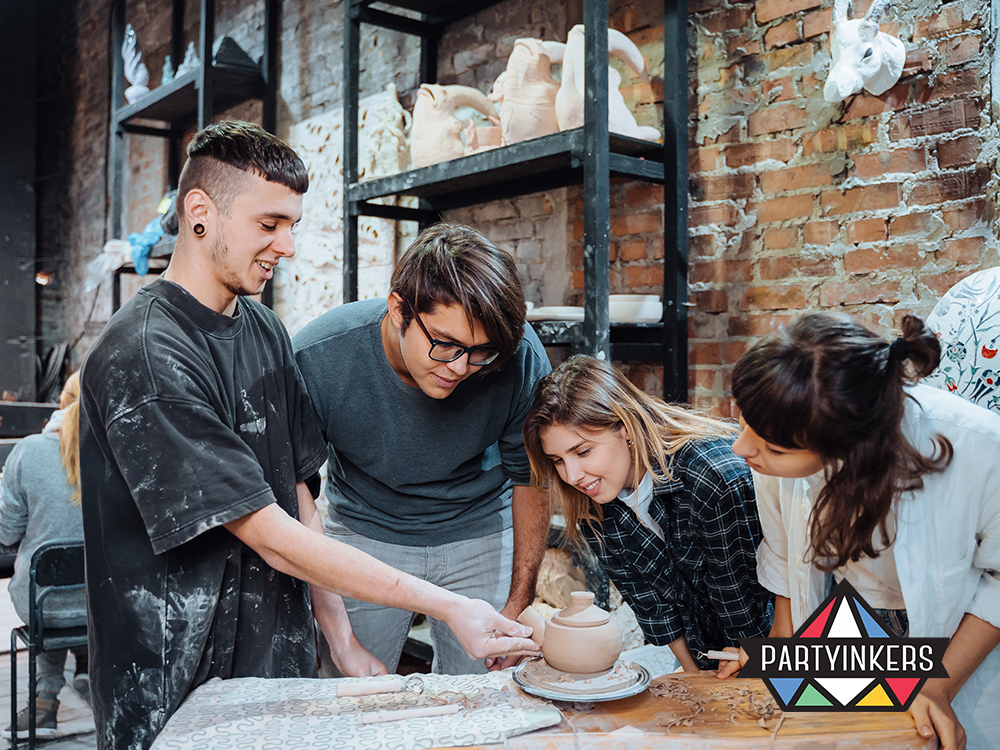 Enthusiastic group of young adults participates in a pottery workshop, closely observing as an instructor demonstrates techniques on a pottery wheel. Set in a rustic studio adorned with artistic creations, the image vividly portrays an engaging hands-on learning experience in ceramic art