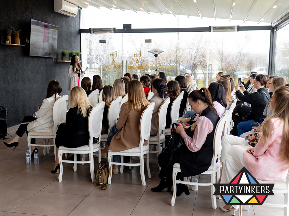 Professional seminar in a modern, glass-walled room with a female speaker addressing an attentive audience of businesswomen. The event setting showcases a sleek, contemporary design enhancing the engaging and educational atmosphere.