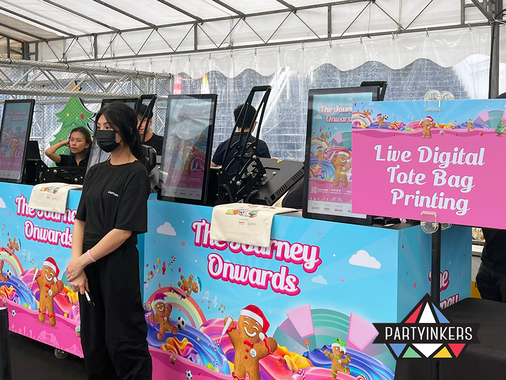 "Colorful booth setup for live digital tote bag printing by Partyinkers at a festive event, featuring vibrant decorations and creative customization options."