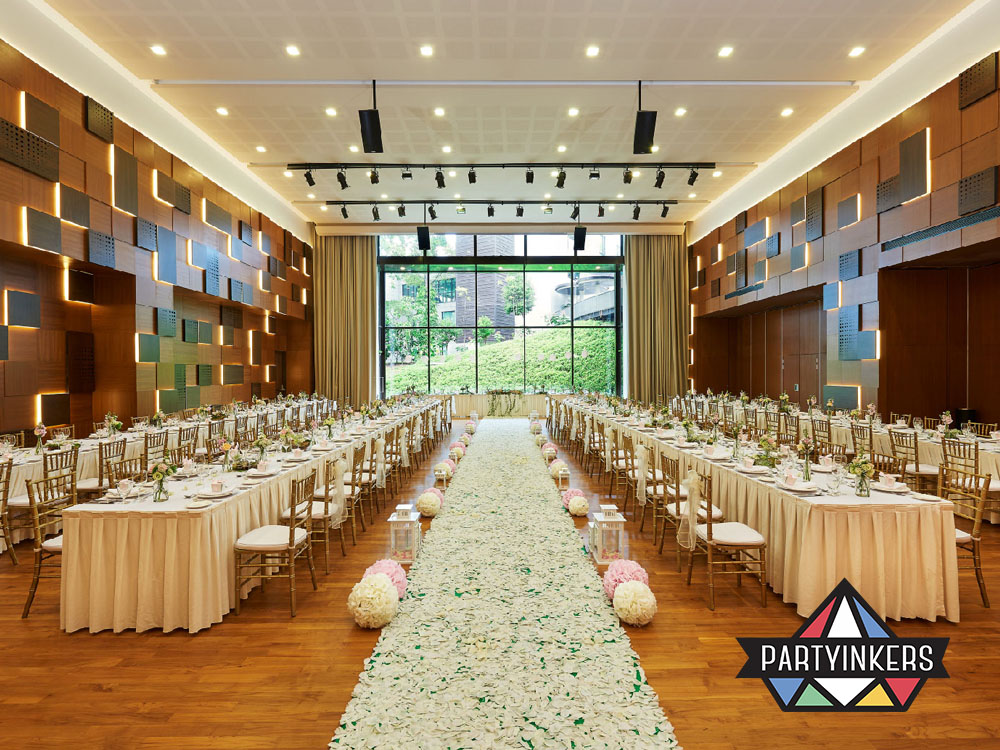 A beautifully decorated banquet hall with long dining tables adorned with floral arrangements, leading to a scenic glass wall overlooking lush greenery.