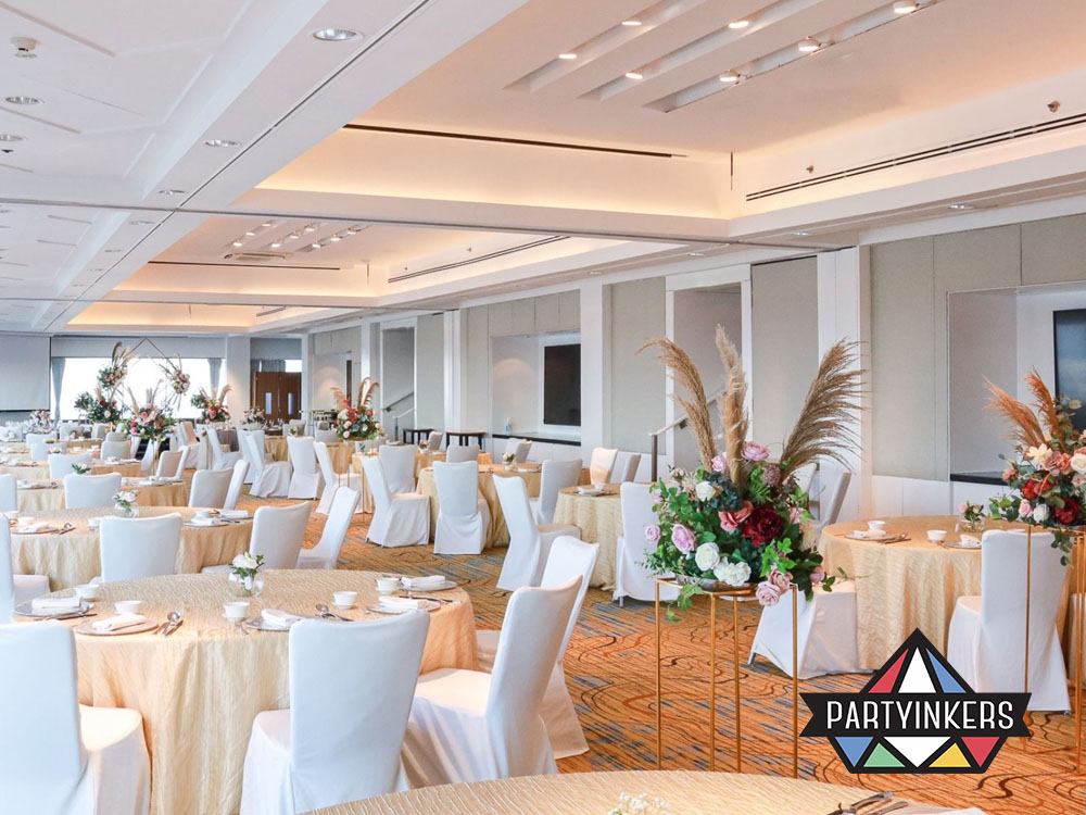 A modern and elegant event space featuring round tables dressed in cream tablecloths, accented with vibrant floral centerpieces and white chairs.