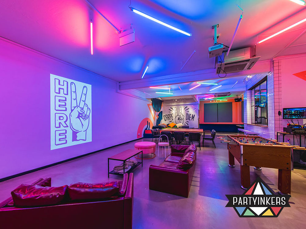 A colorful and dynamic event venue with neon lighting, casual seating areas, and interactive entertainment options like foosball tables.