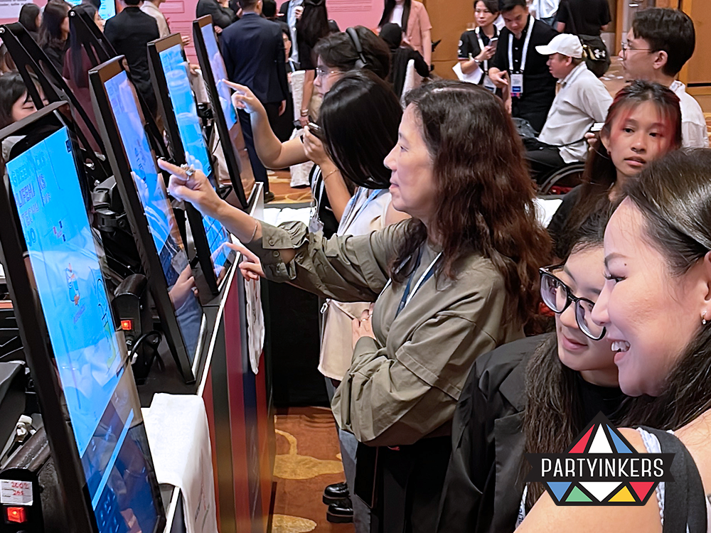 Attendees interacting with touchscreen kiosks at a live event, customizing their designs for on-demand printing. The atmosphere is lively, with participants engaged in a unique hands-on experience, showcasing Partyinkers' innovative and interactive event solutions.