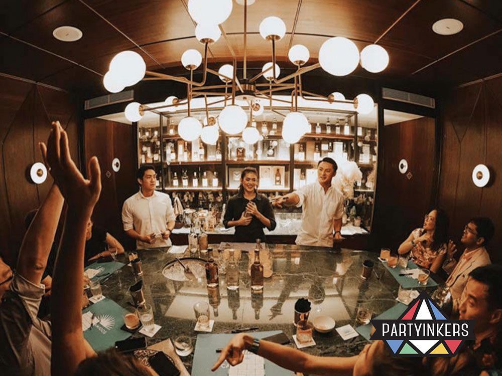 A lively cocktail masterclass in an intimate setting, with attendees engaged around a bar counter under stylish lighting fixtures.