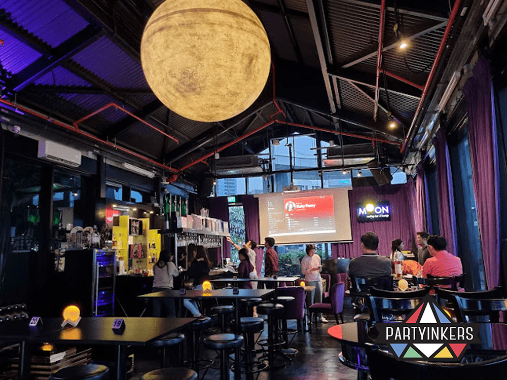 A trendy urban bar with industrial decor, showcasing a relaxed atmosphere and a large moon-shaped light fixture as a centerpiece.