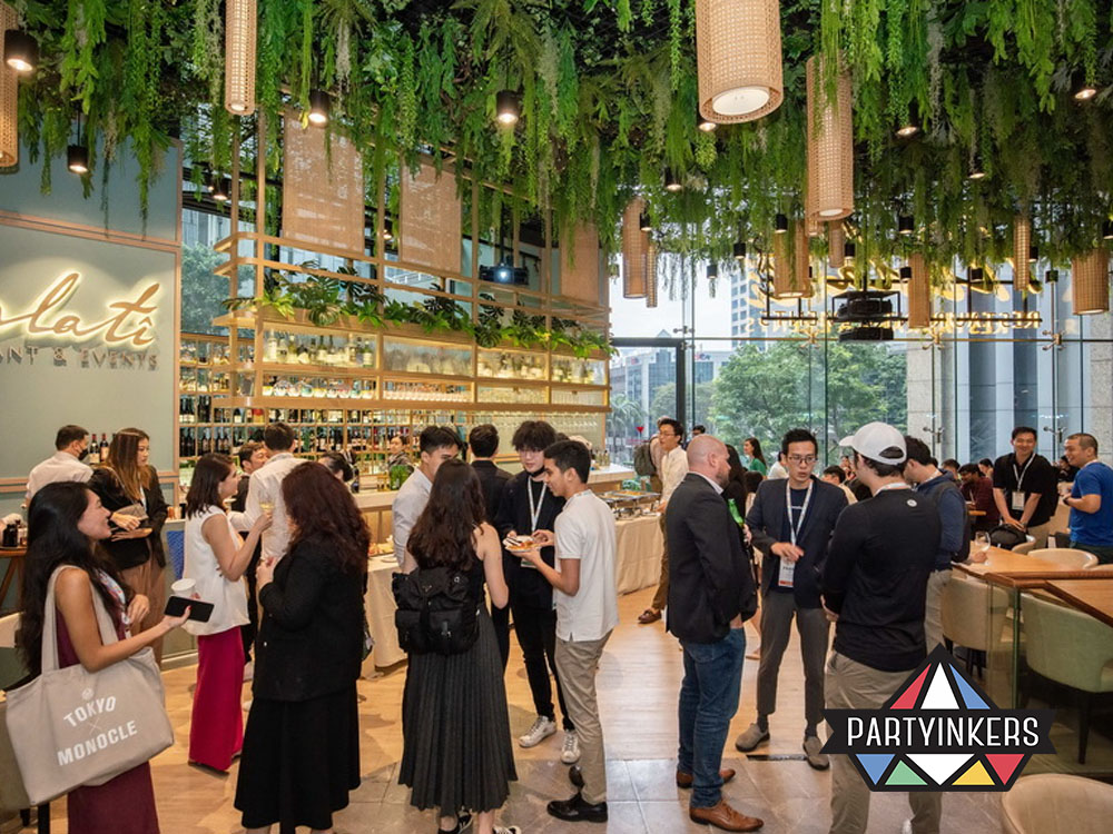 A vibrant networking event at a stylish venue adorned with hanging greenery and a sleek bar area, hosting guests in a professional yet casual setting.