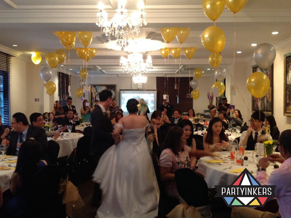 A charming wedding reception with gold and silver balloons, cheerful guests, and a newlywed couple enjoying the celebration.