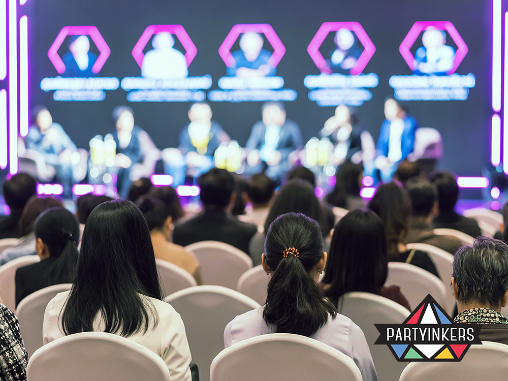 Attendees at a vibrant conference panel discussion, showcasing engaging conference entertainment ideas with a professionally lit stage, dynamic speakers, and colorful digital displays creating an immersive event experience.