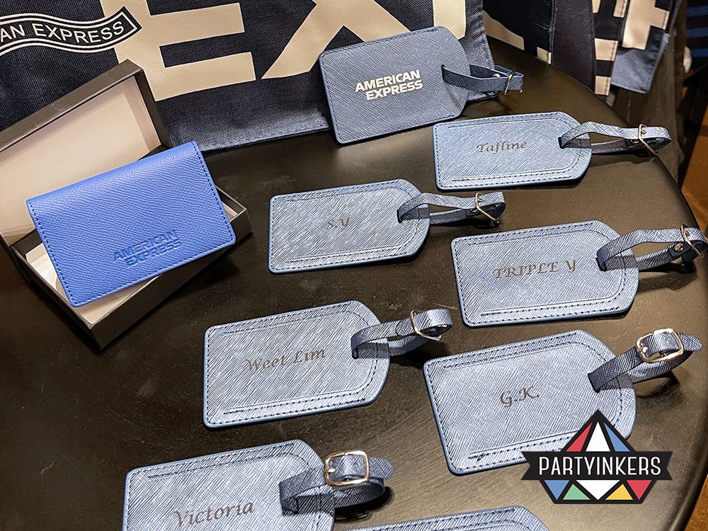 A display of customized blue luggage tags with engraved names, featuring the "American Express" branding at an event booth.
