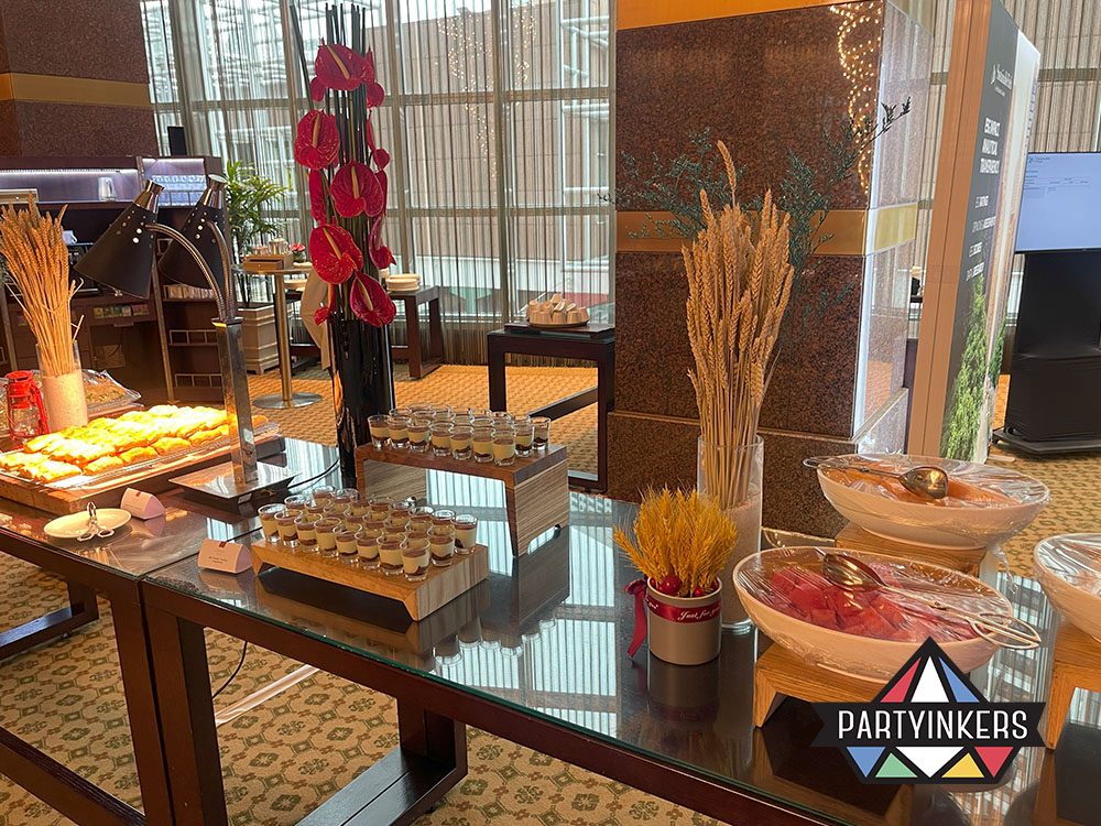 A luxurious buffet setup featuring beautifully arranged dishes, including breadsticks, salads, and desserts, on a glass table with decorative floral accents.