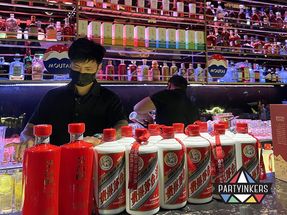 A bartender working at a vibrant bar, featuring an eye-catching display of colorful liquor bottles and a row of Moutai bottles in the foreground.