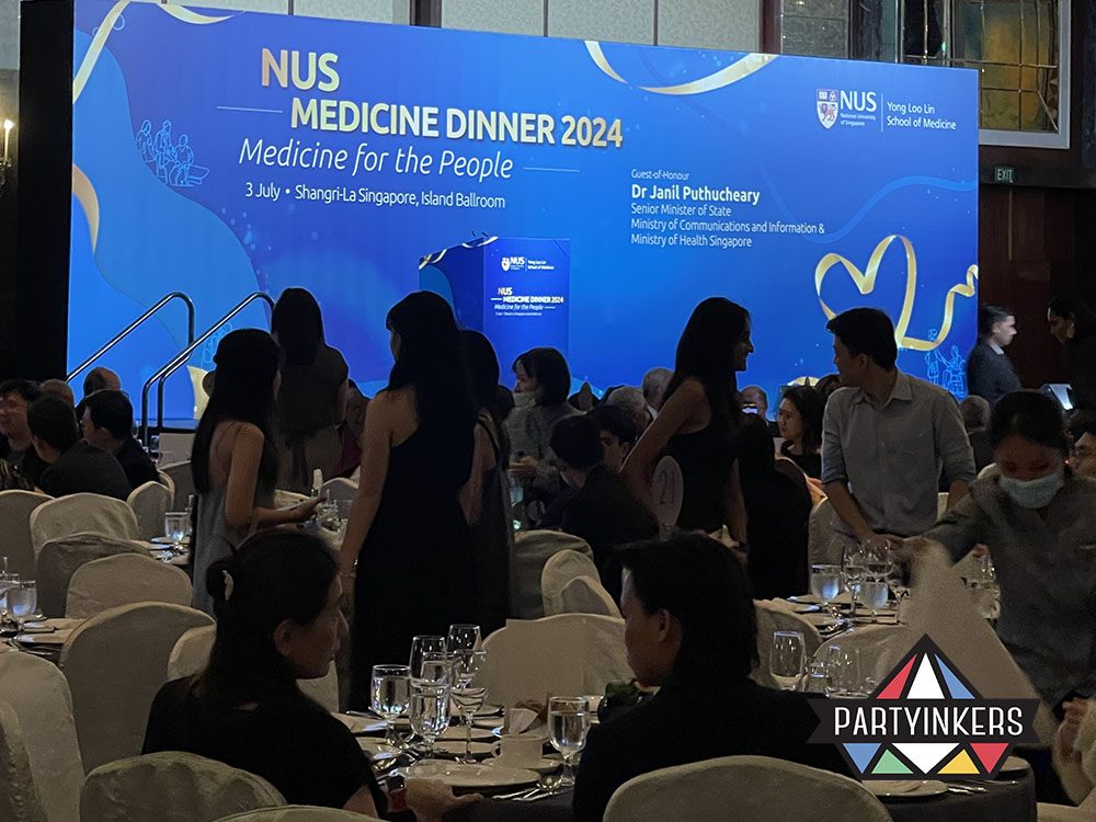The NUS Medicine Dinner 2024 event at a grand ballroom, with guests seated at elegantly decorated tables in front of a prominent stage backdrop.
