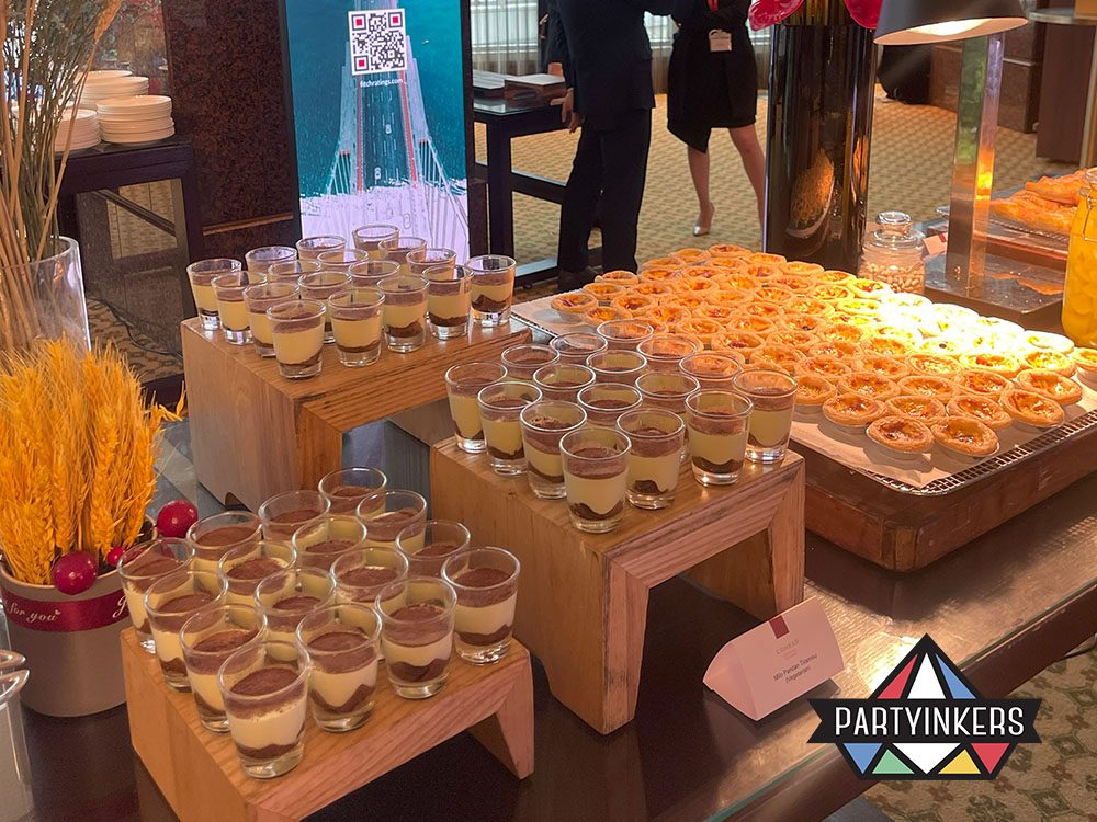 A close-up of a dessert station showcasing an assortment of tiramisu in glass cups and pastries, creatively displayed on wooden stands.