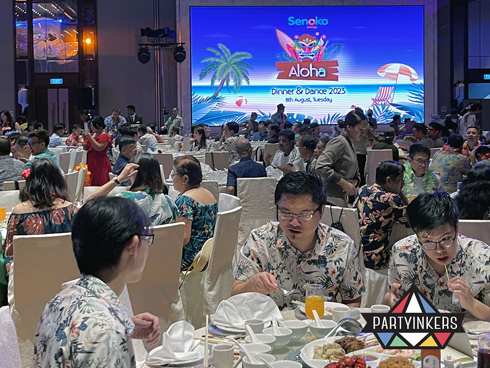 Guests in vibrant Hawaiian-themed outfits proudly displaying their customized tote bags printed live at the event.