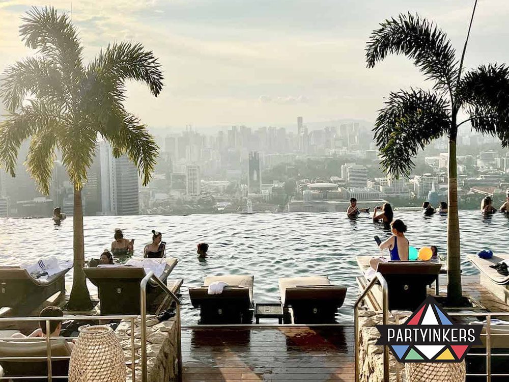 A breathtaking view from an infinity pool overlooking a sprawling cityscape, surrounded by lush palm trees and sun loungers.