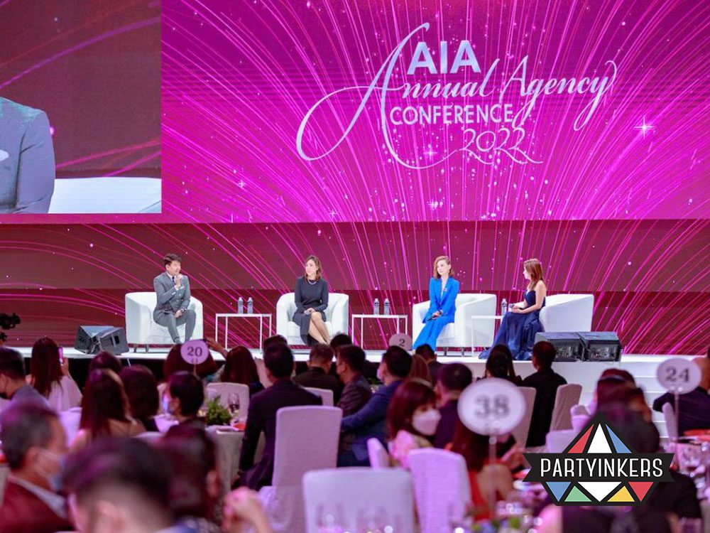 The AIA Annual Agency Conference 2022 featuring a vibrant stage with panelists seated on a well-lit platform and an engaged audience in a grand ballroom.